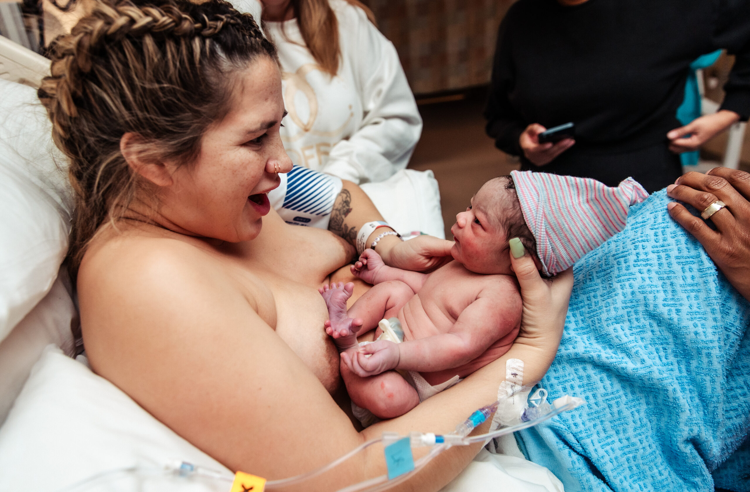 Newborn baby on mother's chest in a hospital room, with other people around.