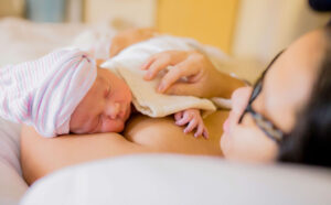 Newborn resting on mother's chest while she touches the baby gently.