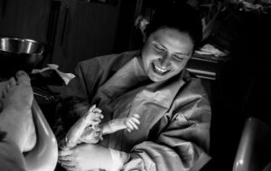 black and white image of a medical professional smiling while deliver a newborn baby