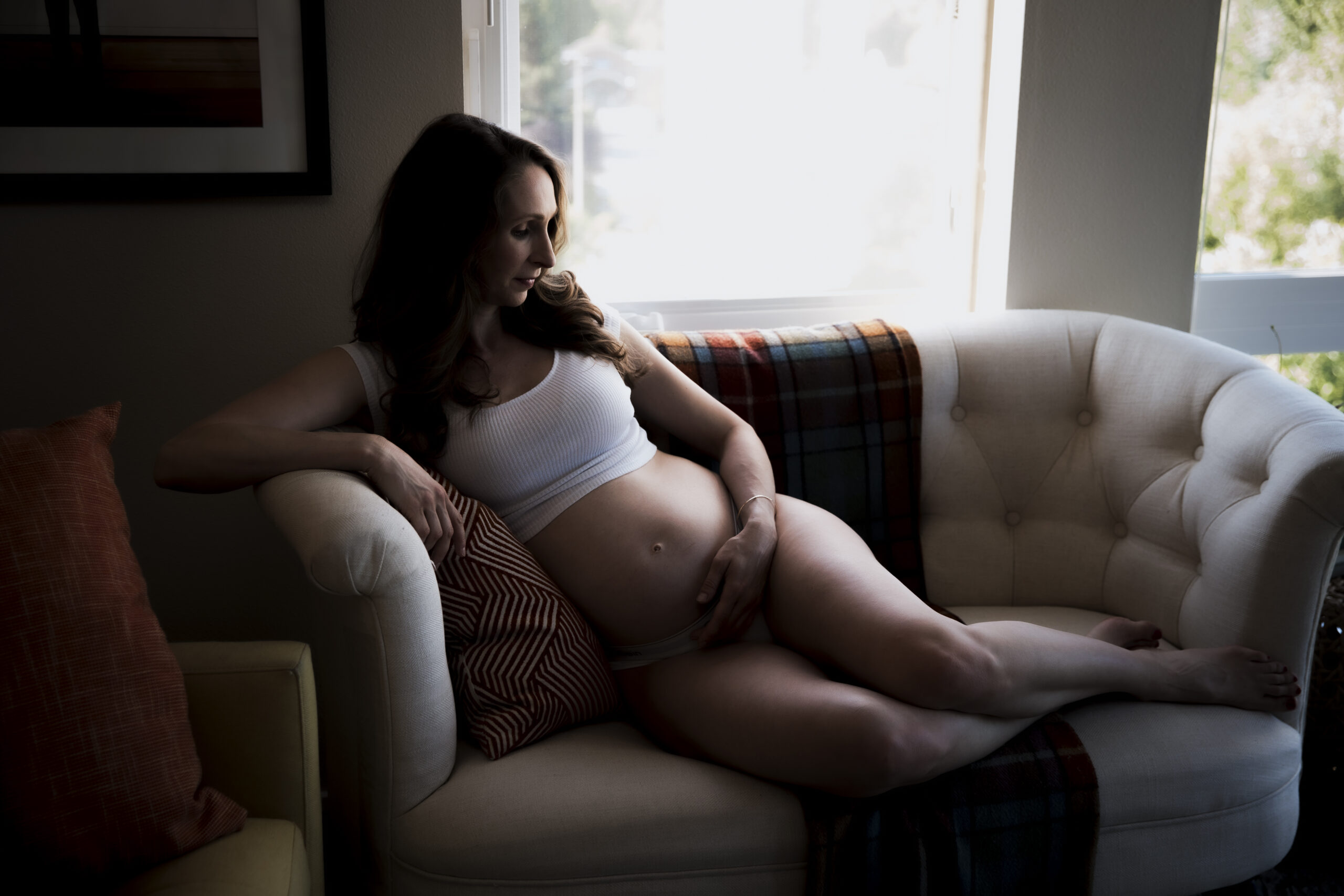 Maternity photograph of a pregnant person lounging on a cozy armchair by a window.