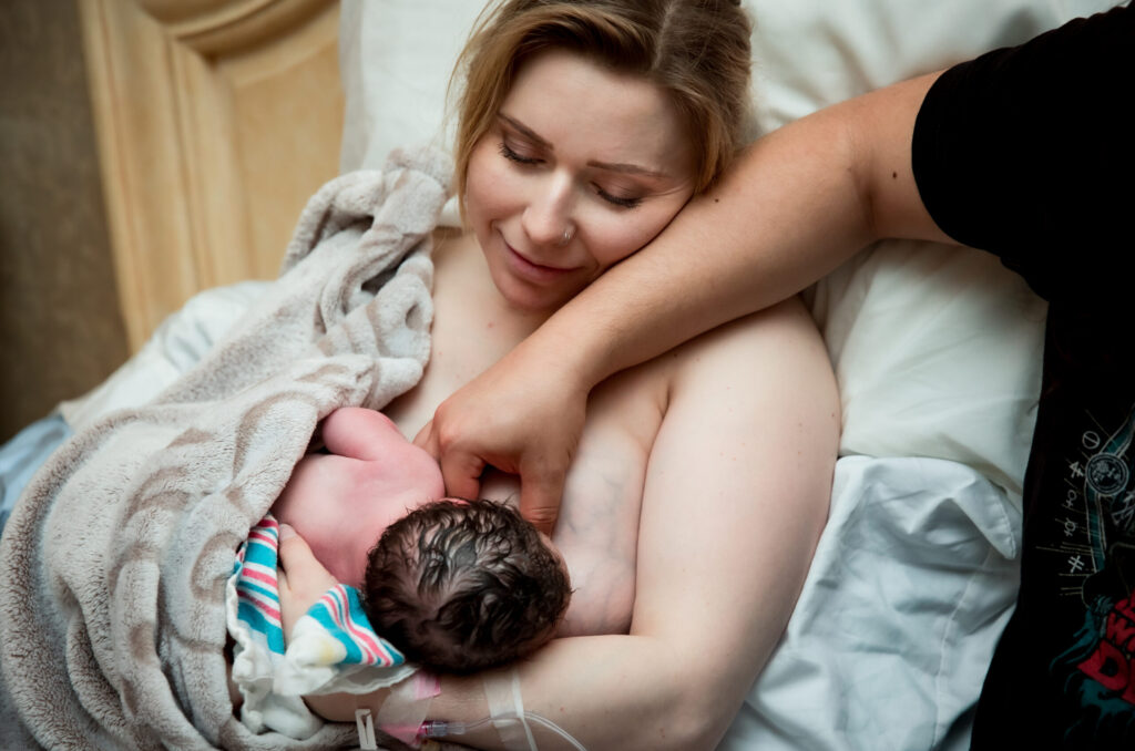 Newborn baby wrapped in a towel resting on an adult's chest.