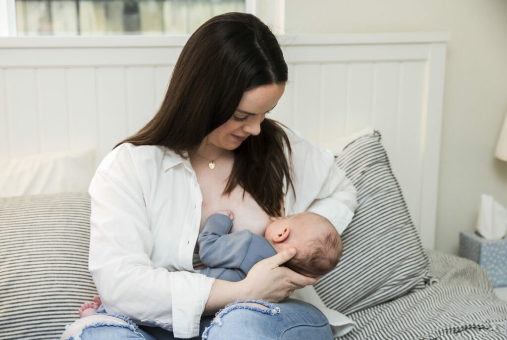 A mother cradling a sleeping baby in a white room with striped pillows.