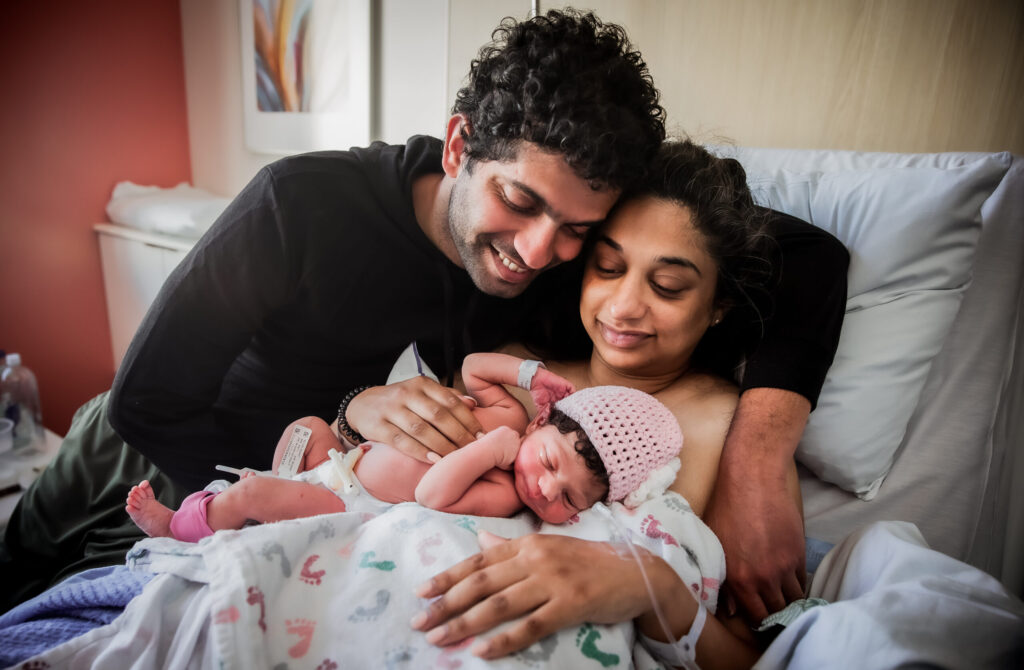 A newborn baby and mother in a hospital bed with another person leaning over them, all sharing a special moment.