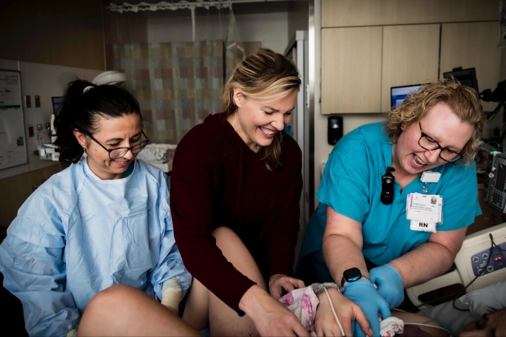 A nurse, doula and parent admire a newborn in a hospital bed