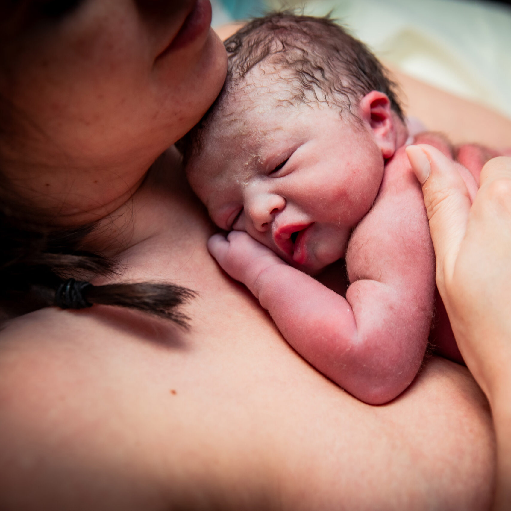 Mother cradling a newborn baby, with a focus on the baby's head and mother's chin.