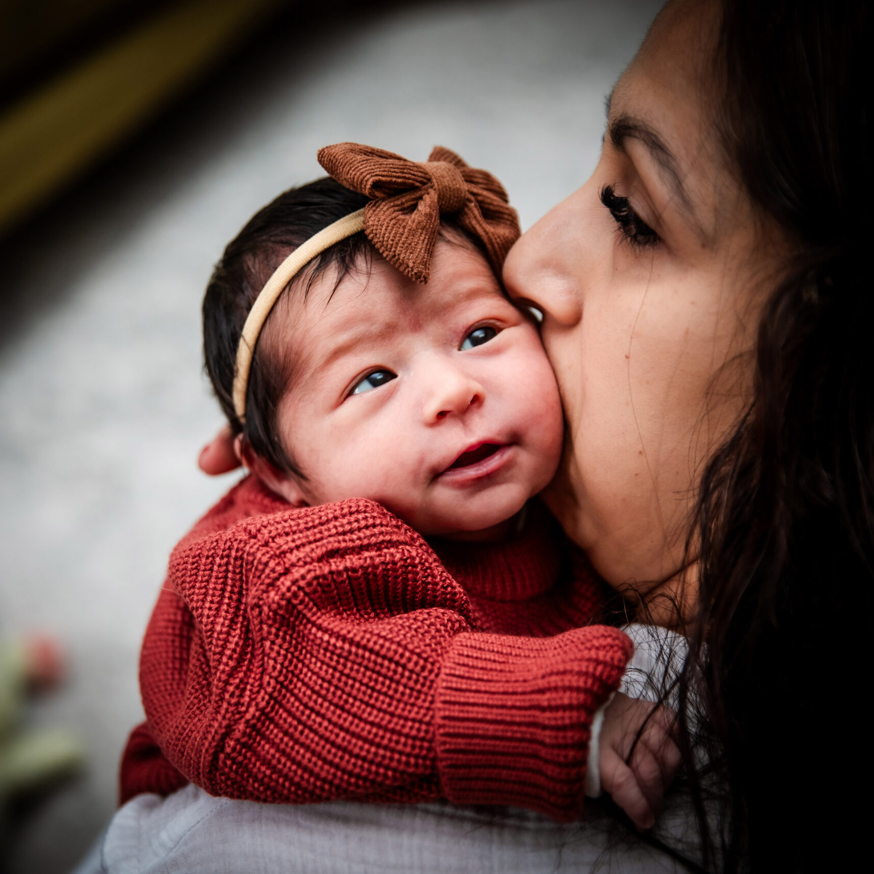 Child in a red sweater resting on mother's should while she kisses the baby's cheek