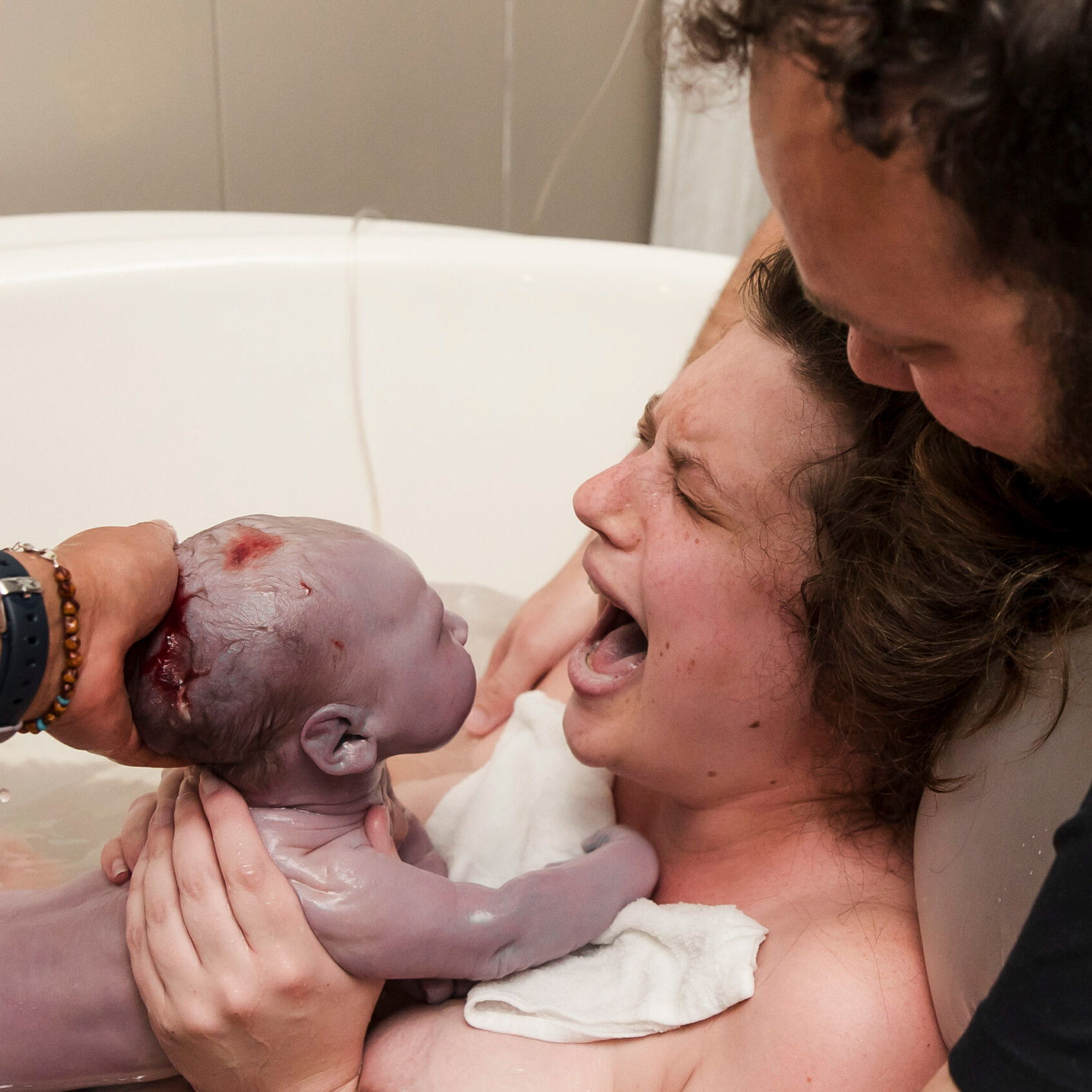 Newborn baby being held in a water-filled tub during a childbirth scene.